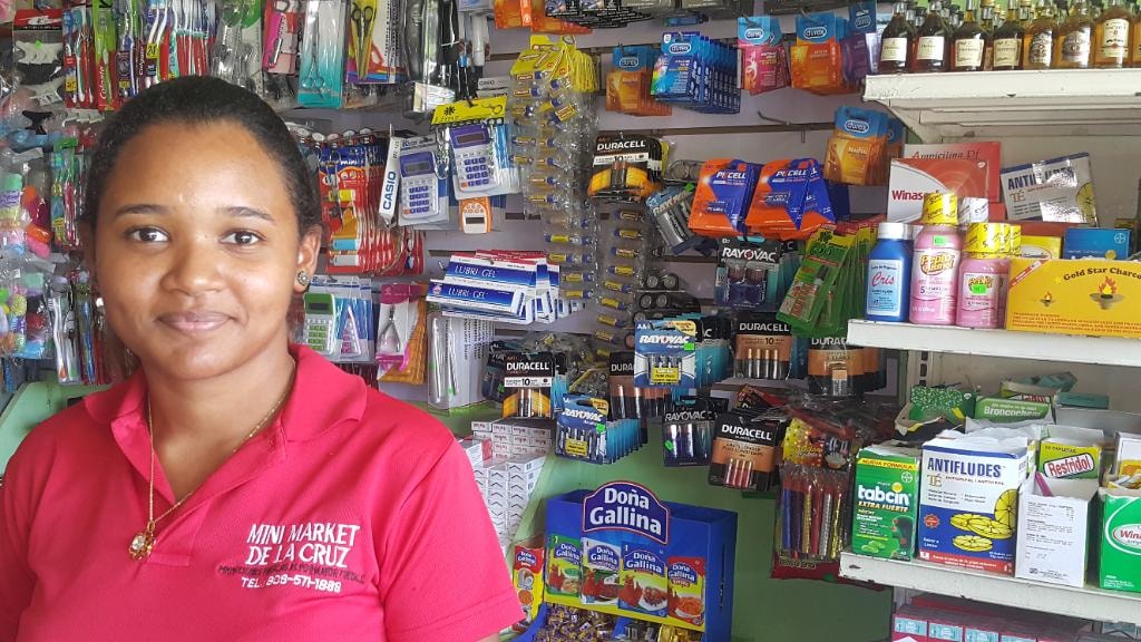 Mini Market De La Cruz staff member with PKCELL battery shelf display